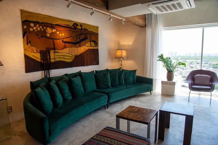 Sala de espera com sofá verde, tapeçaria na parede e janela para a cidade